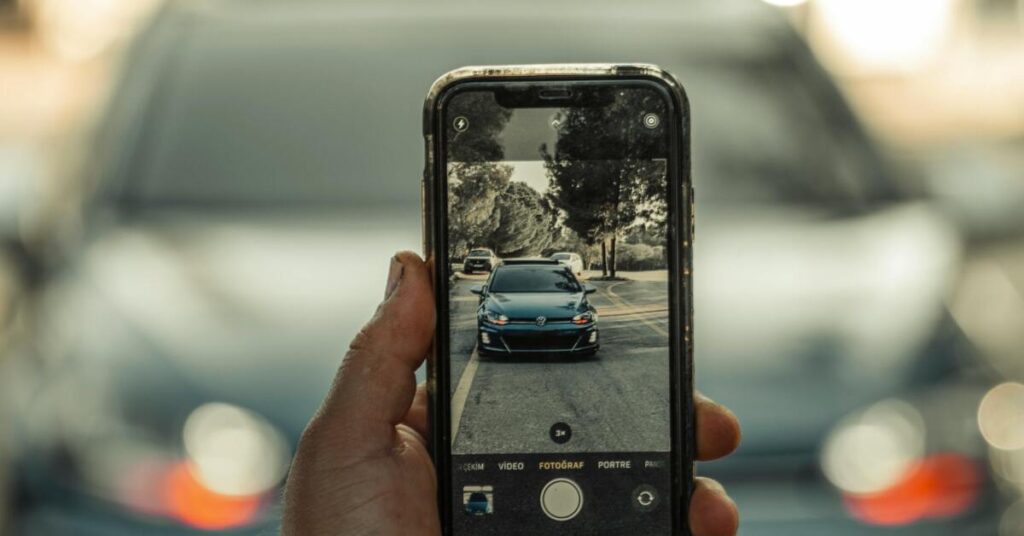 Person using a smartphone to photograph car damage at an accident scene for an insurance claim.